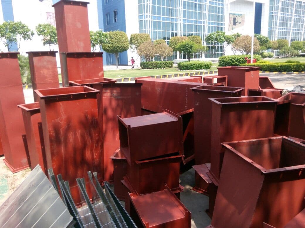 Red-oxide primed MS ducting fittings and collars stacked in the fabrication yard