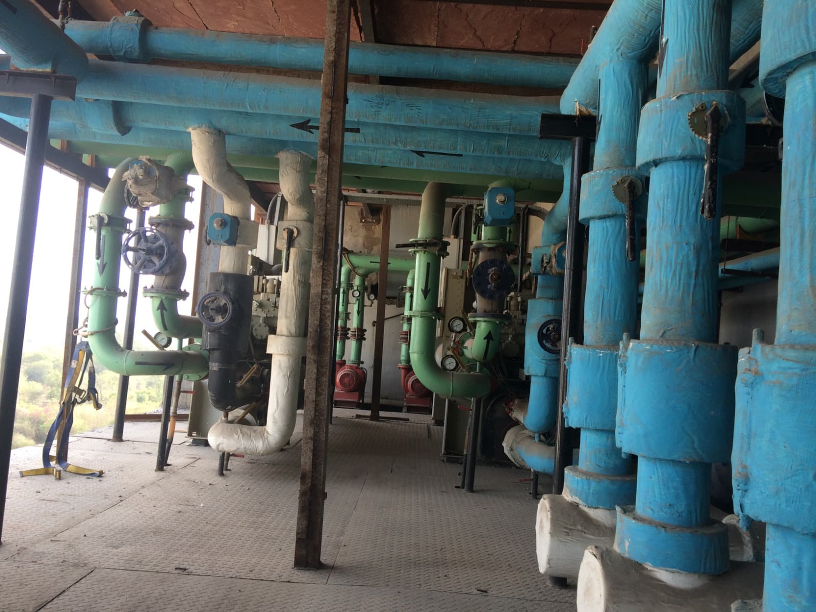 Plant room with insulated green and blue process piping, valves and pressure gauges