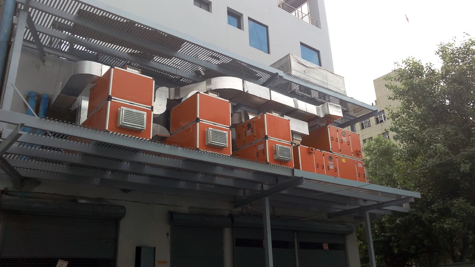 Row of orange treated-fresh-air units with supply ducting on a rooftop deck
