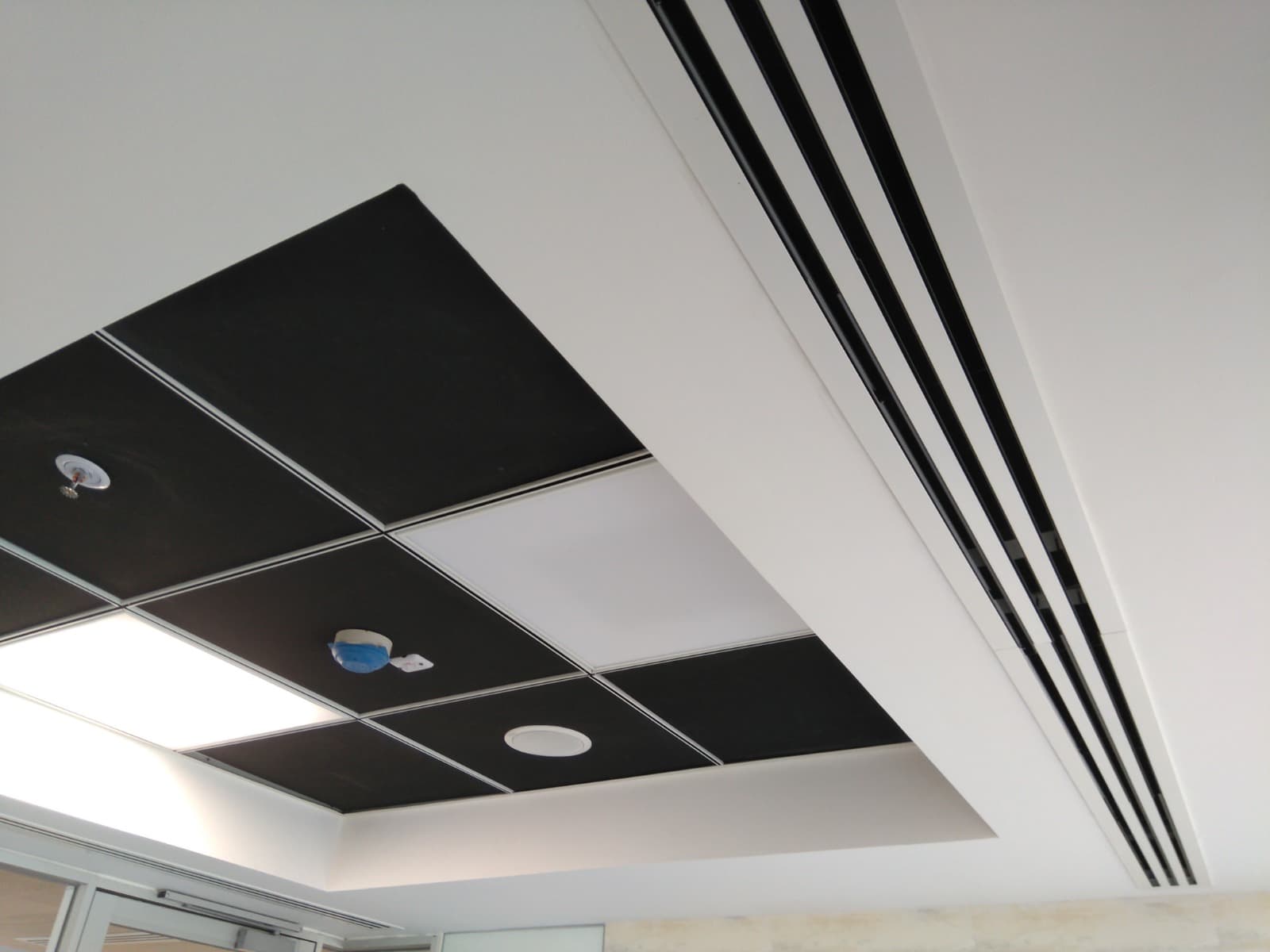 Finished office ceiling with black metal tiles, linear slot diffusers and downlights