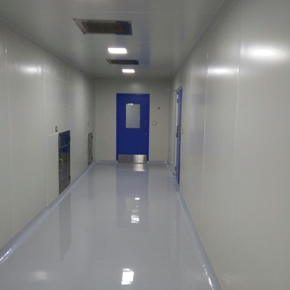 Cleanroom corridor with a blue GMP door, PUF-panel walls and epoxy floor