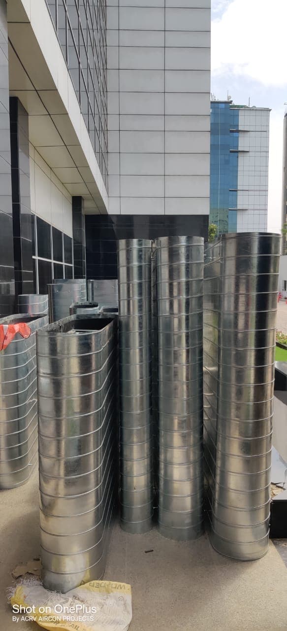 Tall spiral-wound round GI ducting sections stacked outside a commercial building