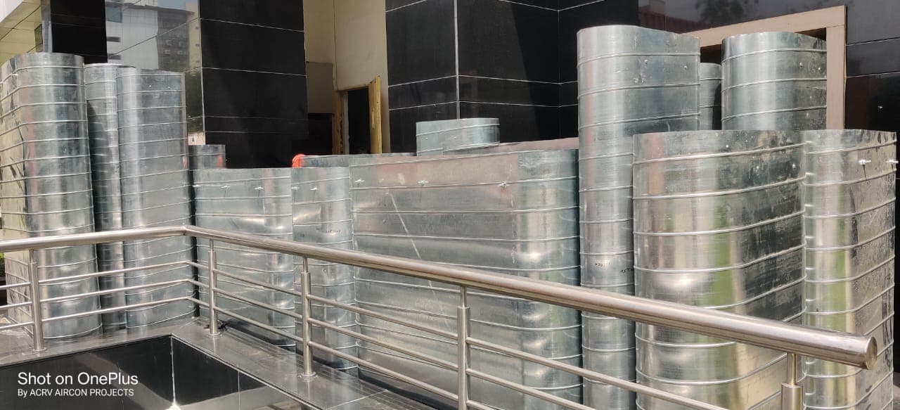 Spiral round and flat-oval GI ducting stacked at a building forecourt