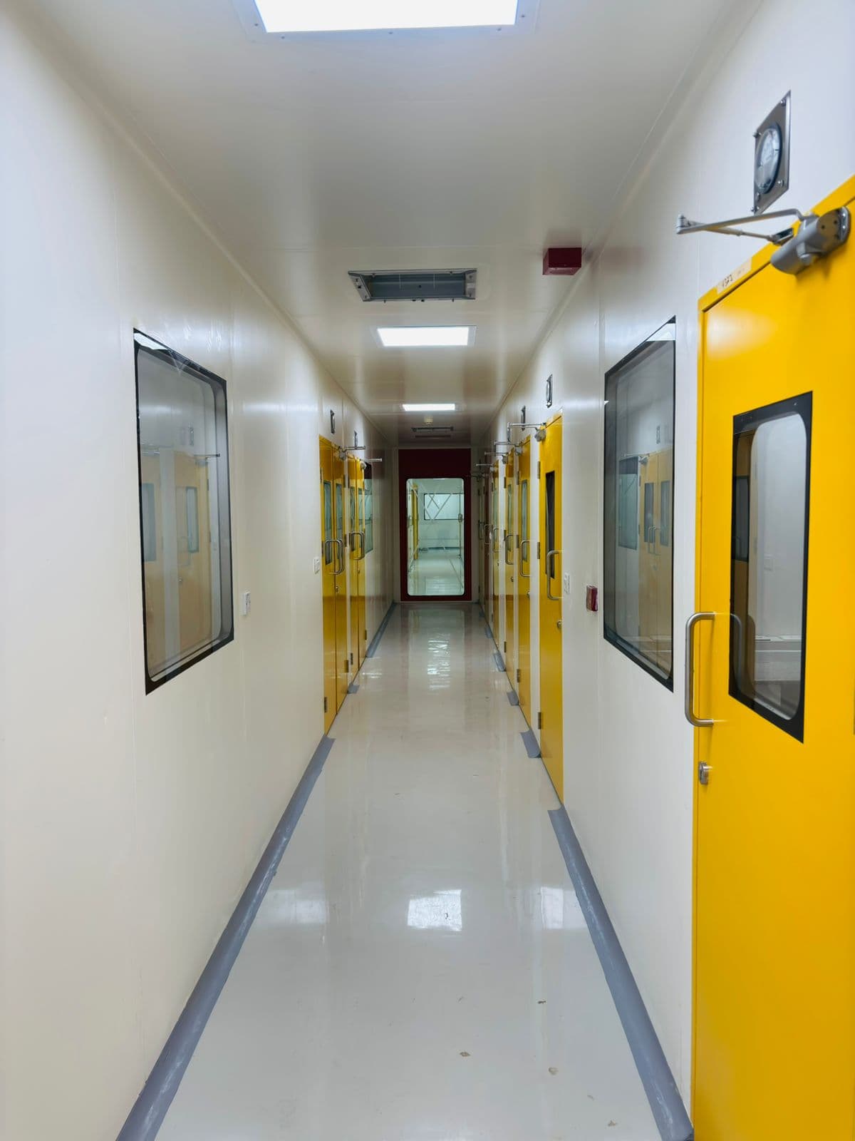 Cleanroom corridor with yellow GMP doors, view panels and pressure gauges