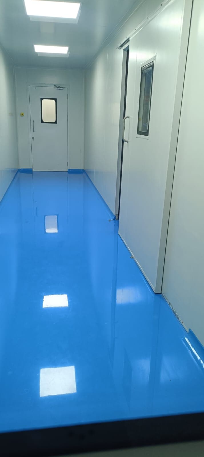 Cleanroom corridor with freshly laid blue epoxy floor and flush GMP doors