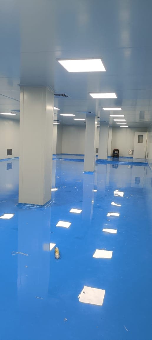 Multi-bay cleanroom hall with blue epoxy floor, PUF-panel walls and return-air risers