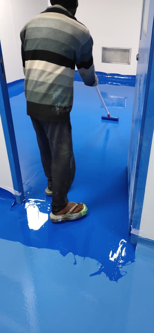 Applying blue epoxy floor coating in a cleanroom with a low-level return-air grille