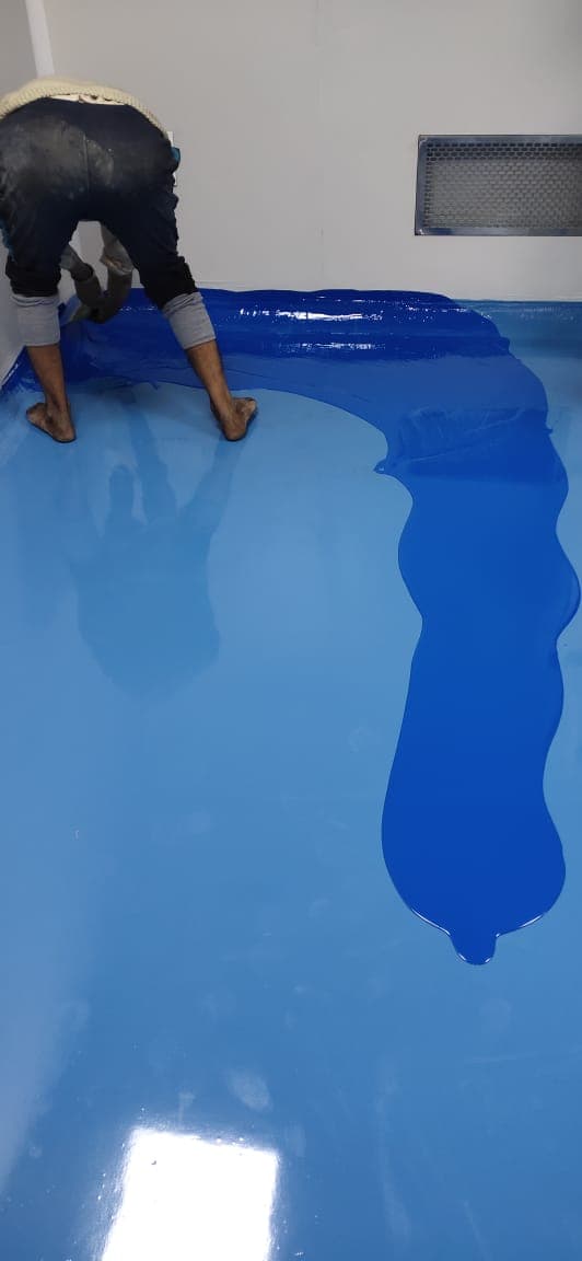 Spreading blue epoxy floor coating across a cleanroom