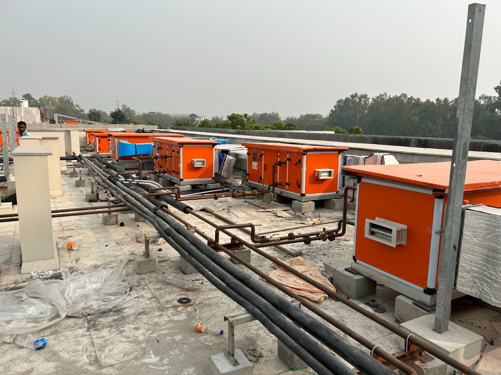 Row of orange treated-fresh-air units with copper refrigerant piping on a rooftop